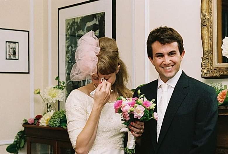 bride crying while holding a bouquet and standing next to groom inside of her parents' house
