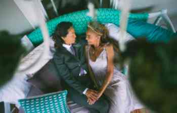 Stylish couple in wedding clothes holds hands and reclines on a green daybed