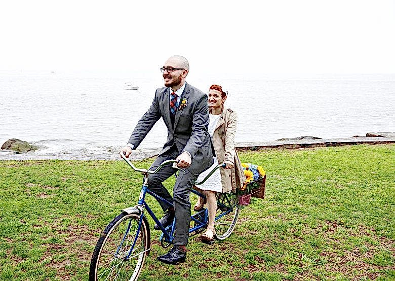 A couple on a tandem bike riding up to their backyard wedding