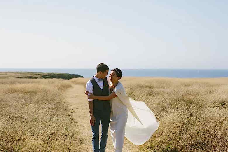 bride and groom in field in front of ocean on their wedding day
