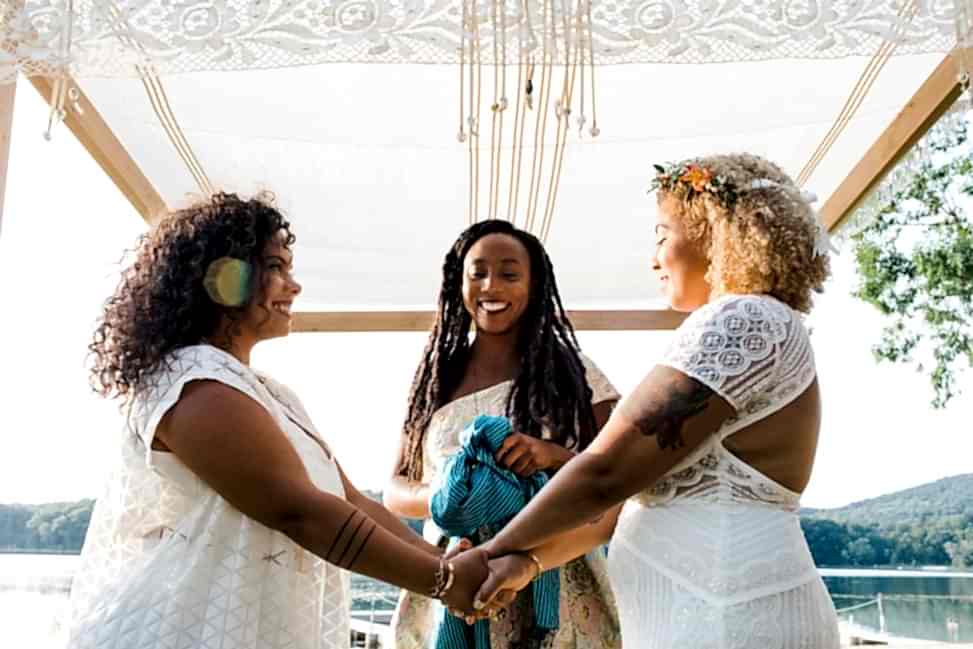 Two brides hold hands under a chuppah