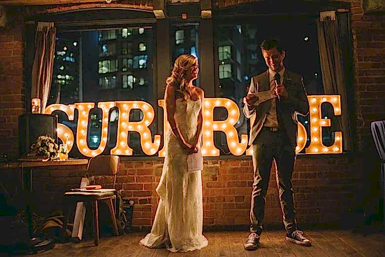 bride and groom speaking in front of surprise sign
