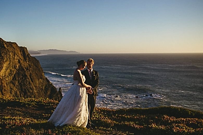 Bride and groom standing together in front of the ocean