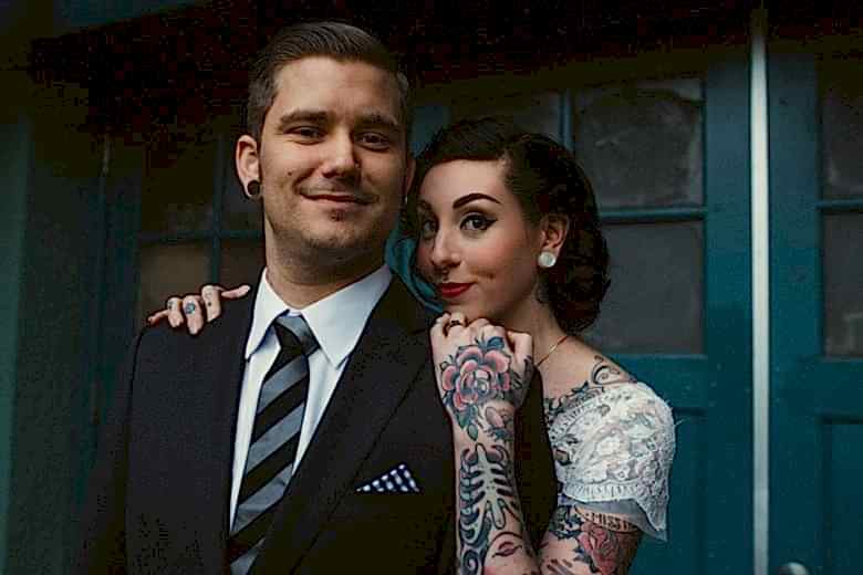 tattooed bride and groom standing in front of blue door