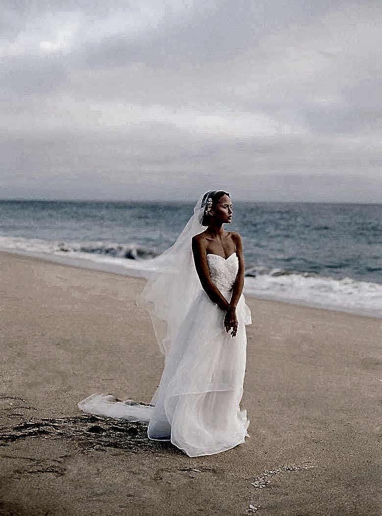 girl in white bridal outfit looking out over ocean
