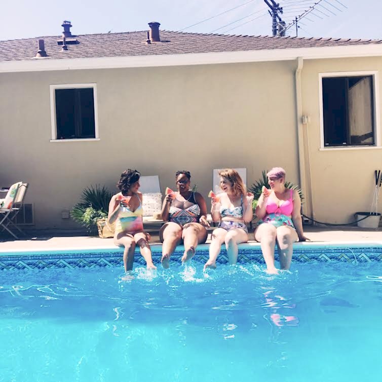 Four women sitting by the edge of a pool with drinks