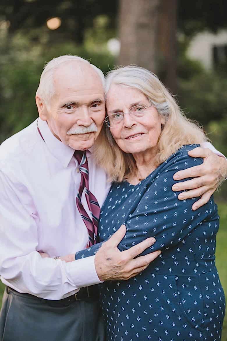 older man in pink shirt and woman in navy blue embracing