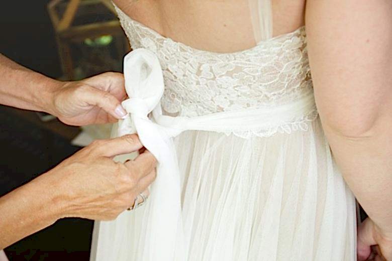 mother tying sash on daughter's wedding dress