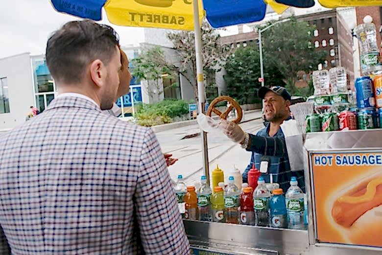 two grooms buying a pretzel from a street vendor