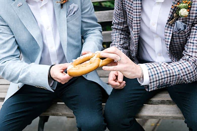 hands of two grooms holding pretzel