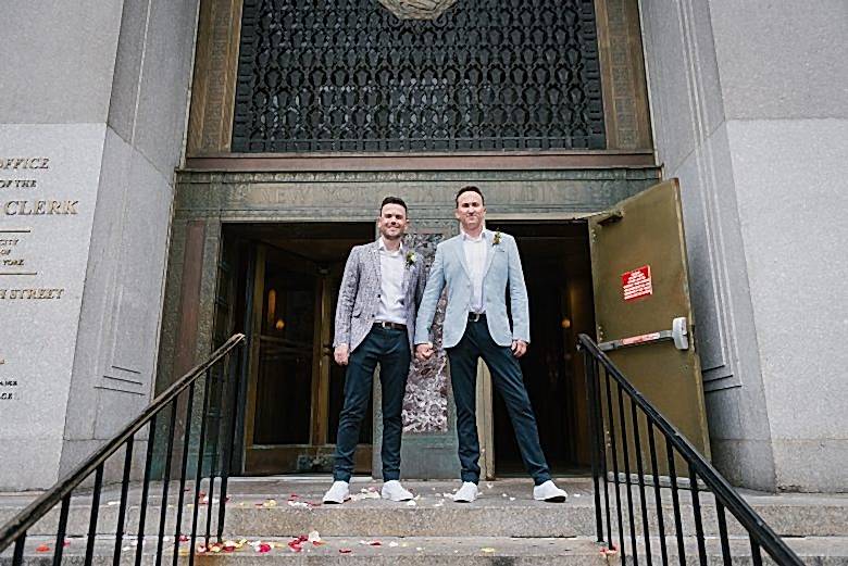 two grooms in front of the doors to New York City Hall