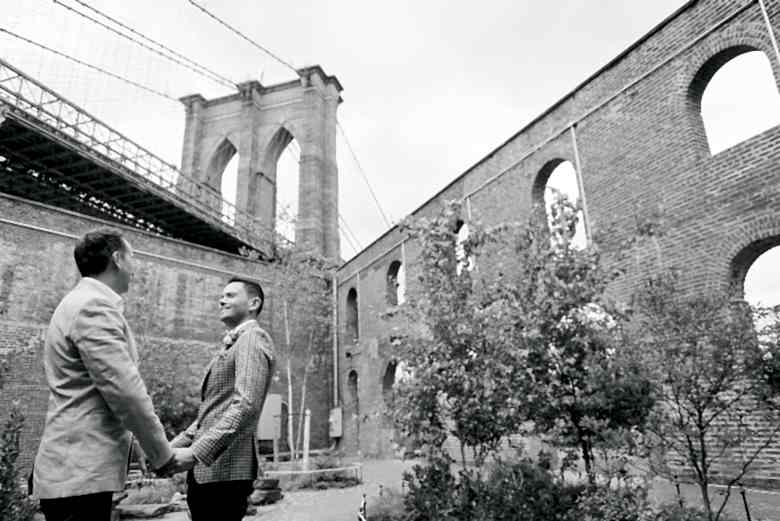 black and white portrait of two grooms at base of brooklyn bridge