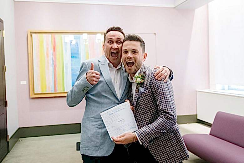 two grooms in New York City Hall with marriage certificate