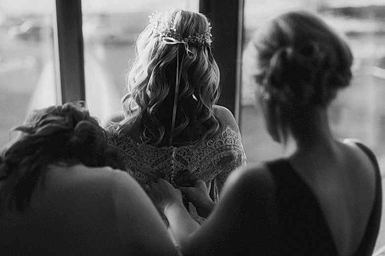Women buttoning bride's dress