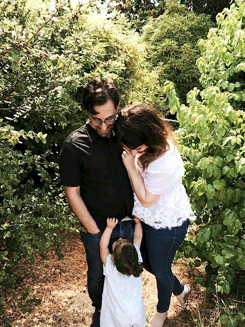 author and her husband looking down at a toddler in front of greenery