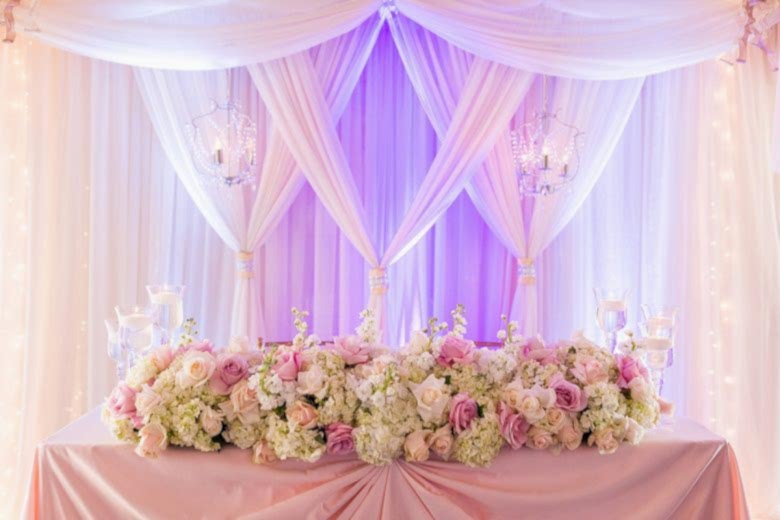 Sweetheart table with flower arrangements and draping with uplighting