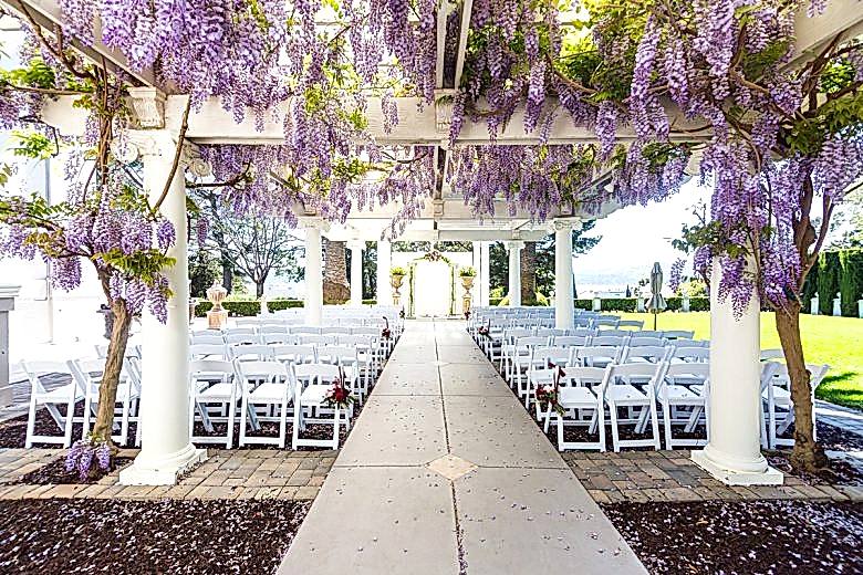 Ceremony venue with white chairs and wisteria on a pergola overhead