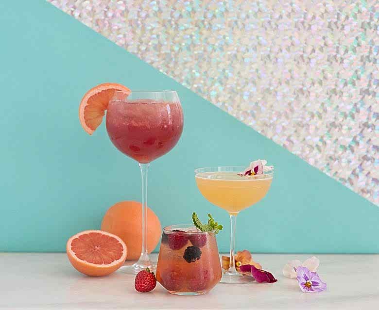 APW + Crate and Barrel + Lo-Fi Aperitifs three cocktails with fruit and flower garnishes