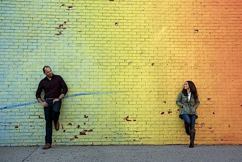Couple standing in front of ombre blue-green-yellow-orange brick wall