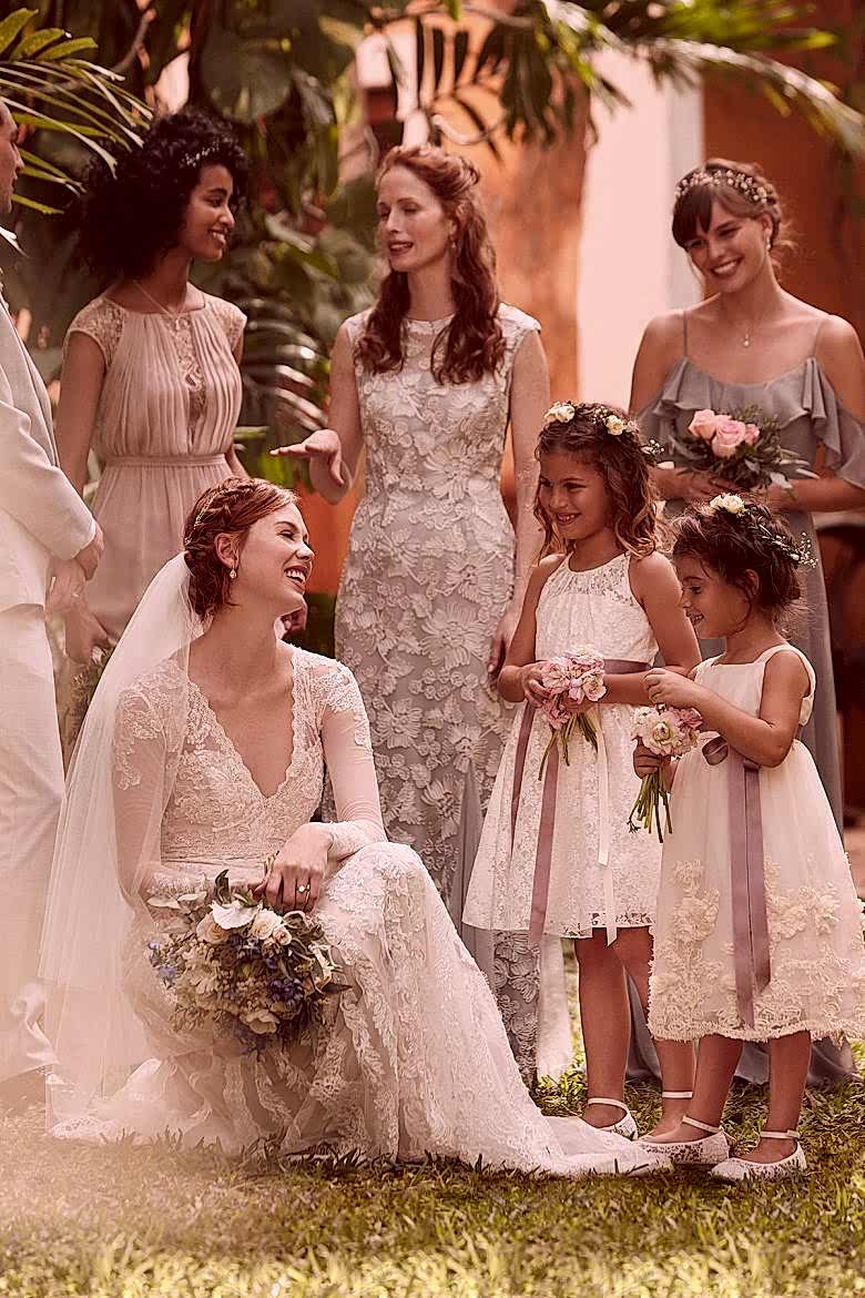 Woman wearing Linear Lace Wedding Dress, holding bouquet, with three women in bridesmaid's dresses and two girls in flower girl dresses
