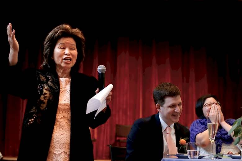 Woman at microphone giving toast while people laugh