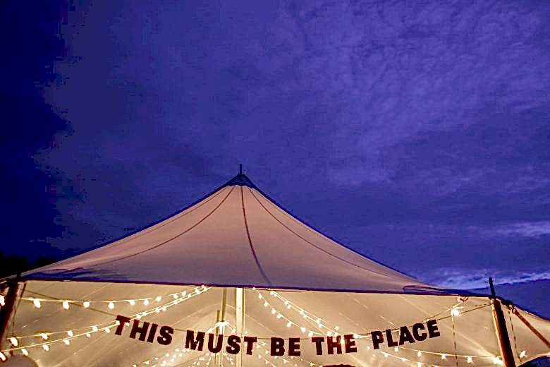 Party tent illuminated with white string lights with a banner that reads "This must be the place"