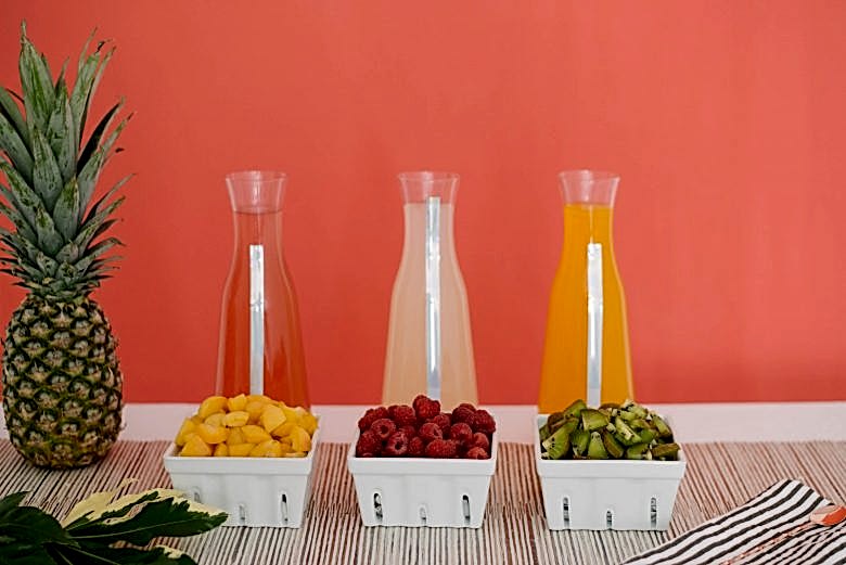Three carafes of juice with three ceramic berry baskets with fruit, and a pineapple 