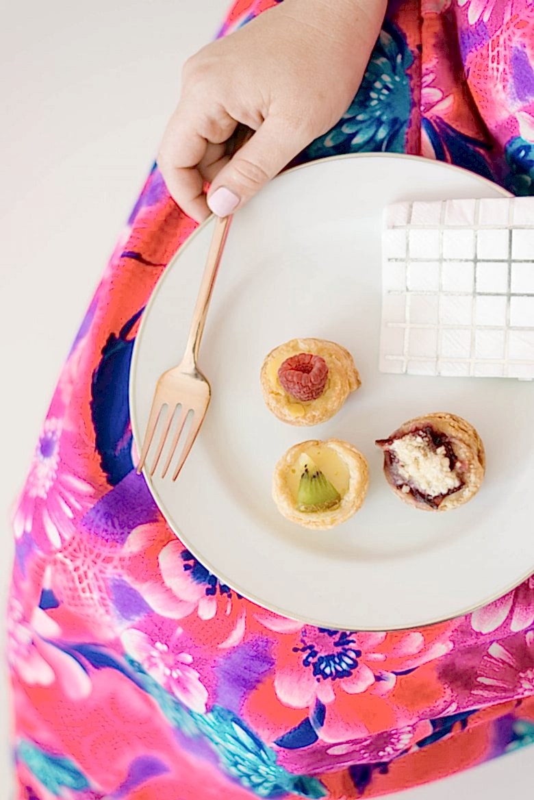woman in bright floral dress holding plate with mini pies and copper fork on her lap