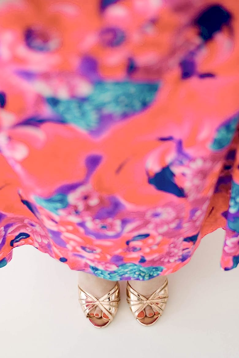 Feet of woman in brightly colored floral dress, wearing shiny gold open-toed sandles 