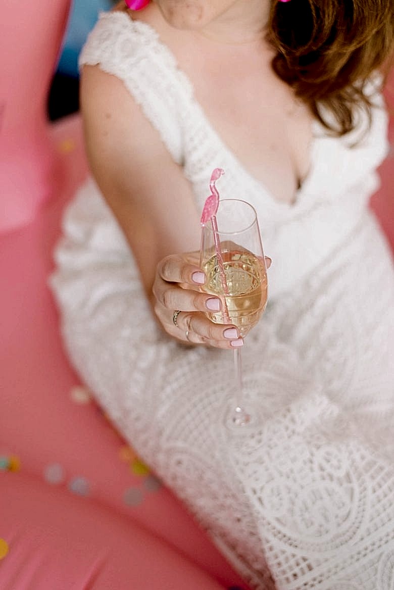 Woman in white holding champagne flute with pink flamingo swizzle stick