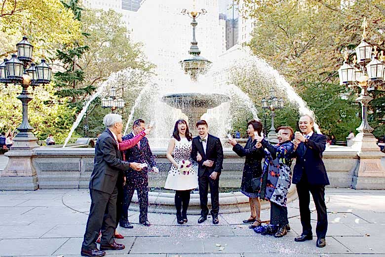 Couple, with their families, being showered in confetti in front of a fountain