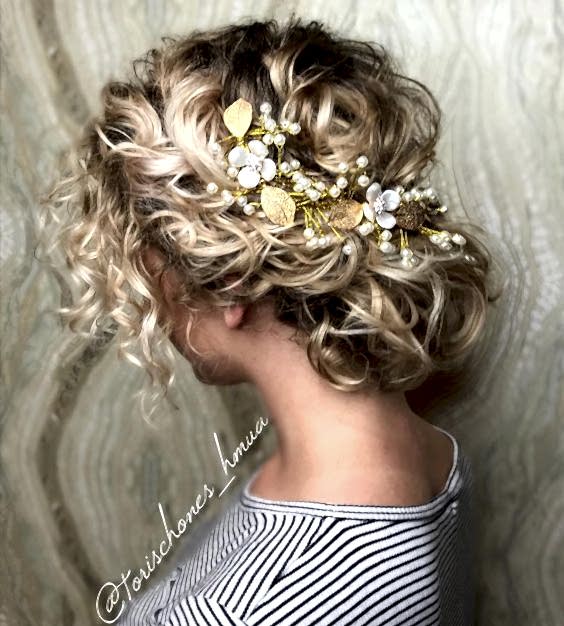 blond curly hair gathered low at the nape of her neck, with gold leaf, pearl, and white enameled flower hair accessory