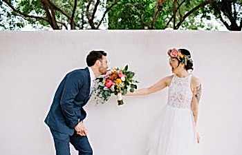 Groom playfully bites at brides bouquet as she laughs