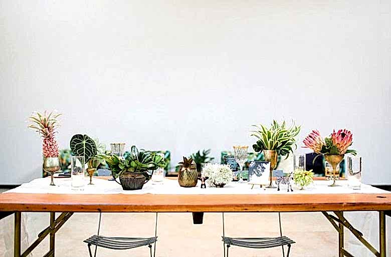 tablescape with tropical-looking plants and flowers in various metallic containers, with small zebra