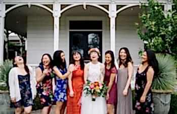 A bride smiles and laughs as she is surrounded by her wedding party