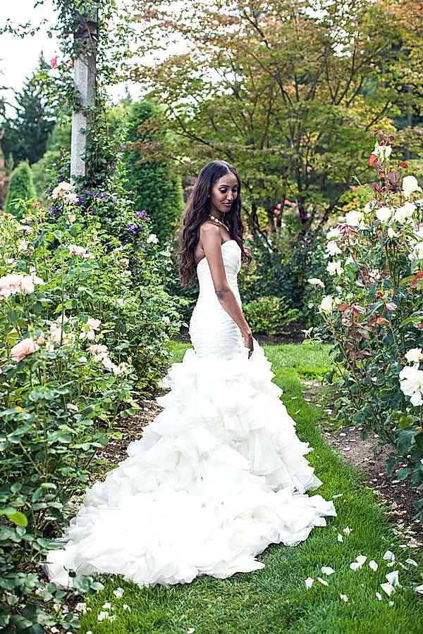 woman in rose garden with long cascading strapless white wedding dress with long dark, wavy hair parted down middle
