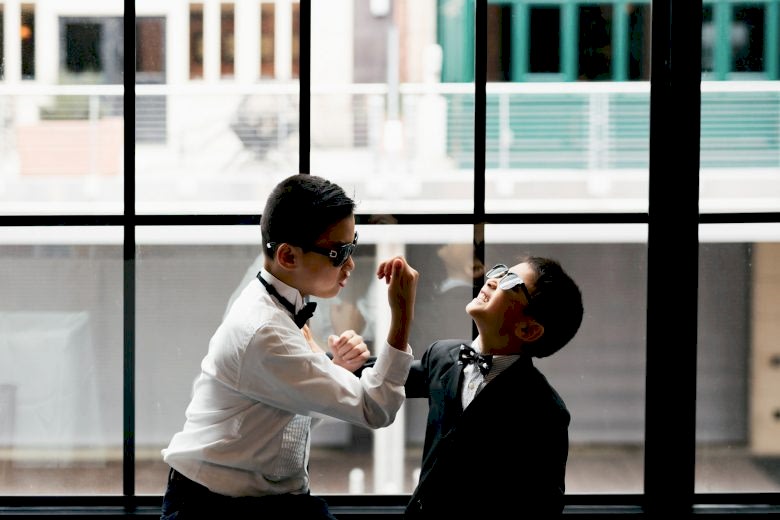 Two young boys in boy ties and glasses playing around in front of warehouse style window