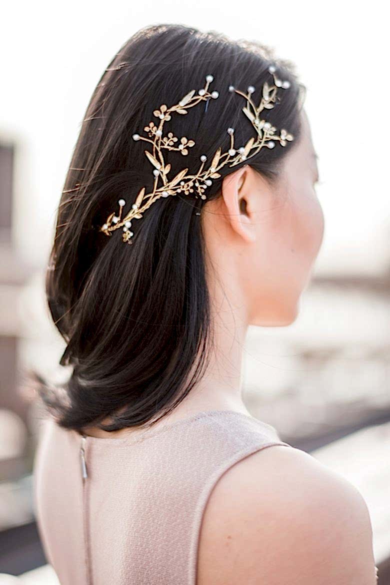 woman with sleek dark shoulder-length hair with the right side secured with a gold and pearl leaf and flower headpiece