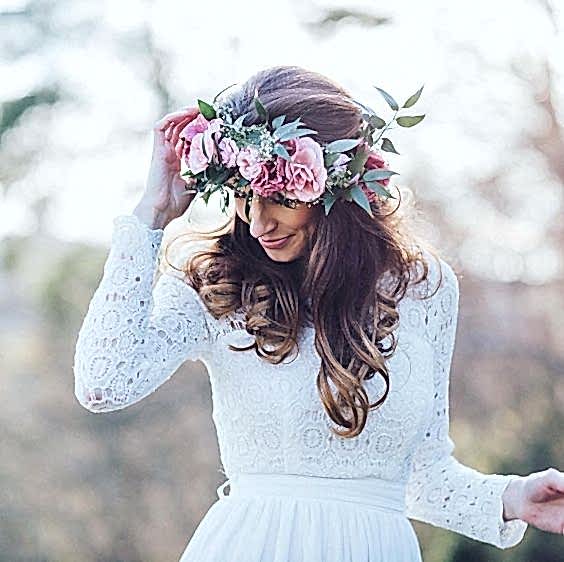 woman in white crochet lace–top wedding dress with long brown soft curls and a large pink and green flower crown