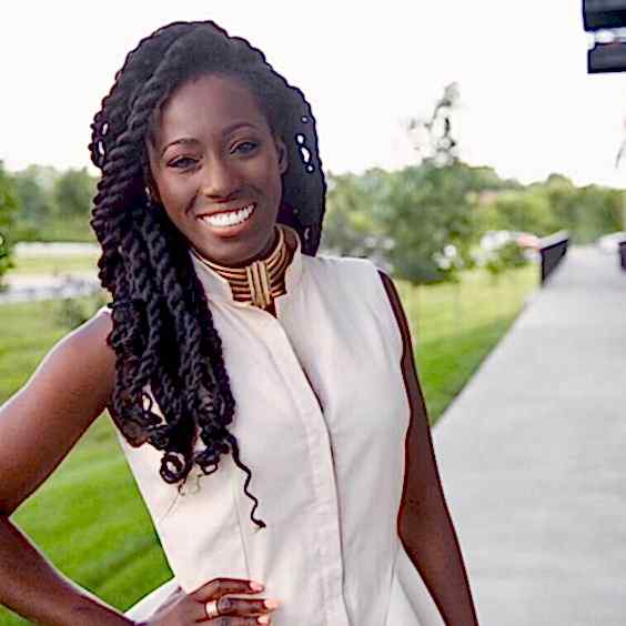 Woman smiling in white dress with wide gold choker and long dark hair styled into many thick twists