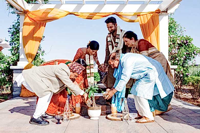 Family members planting and watering tree in small pot with bride and groom