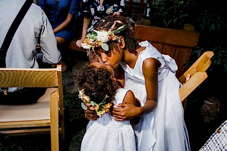 Two flower girls in white dresses with flower crowns kissing