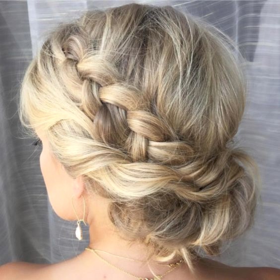 woman with a loose braid along left side of head with another layer of hair woven along underneath, gathered in the back