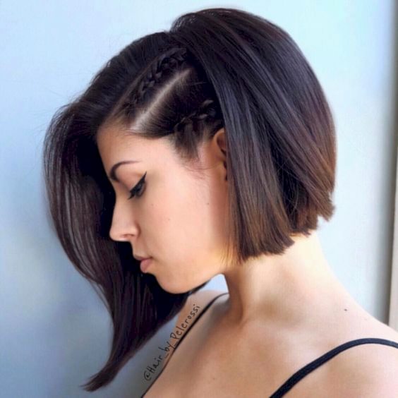 woman with dark hair in chin-length bob with the front left half tightly braided into two thin dutch braids with dramatic parts