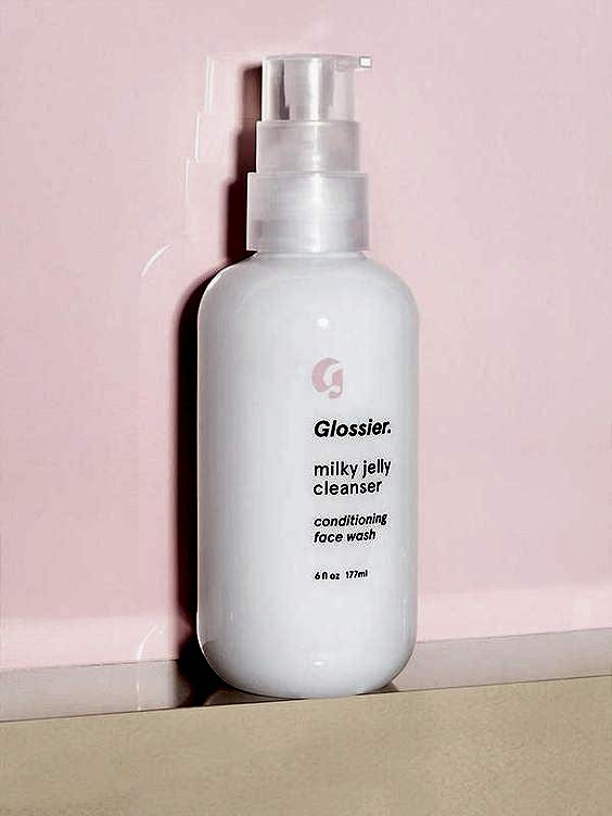 Glossier milky jelly cleanser bottle sitting on shelf against pink background