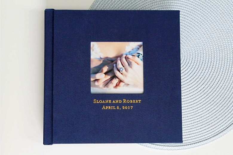 Dark blue square hardcover album with photo inlay and debossed gold type reading Sloane and Robert April 8, 2017
