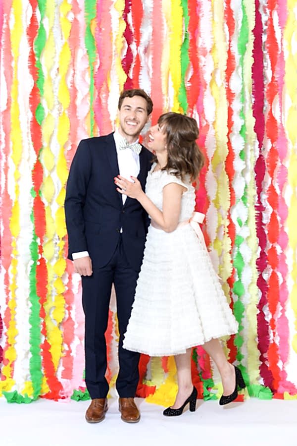 Bride and groom standing in front of a fringe streamer background wedding decoration.