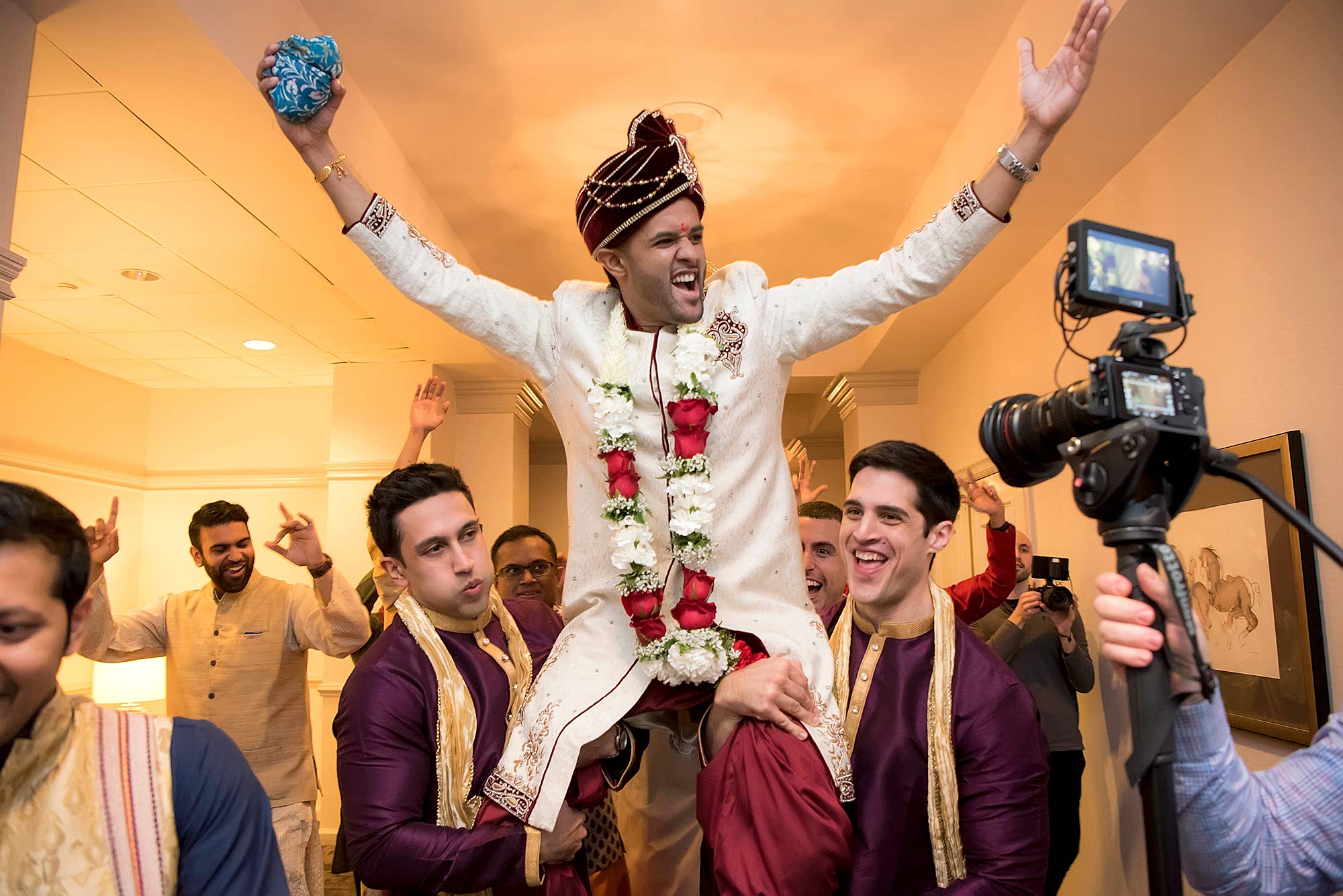 A groom is lifted up on the shoulders of his friends.