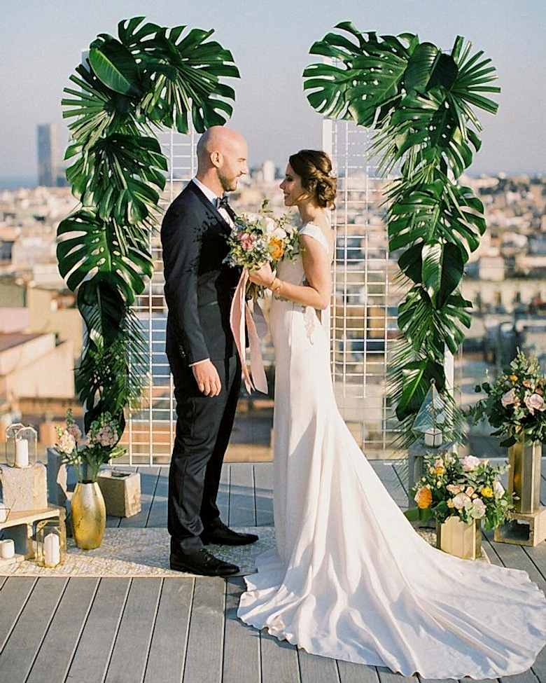 bride and groom at altar overlooking a cityscape bordered by large tropical leaves