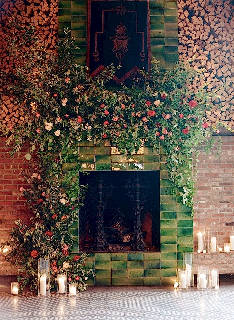 lush flowers and greenery overflowing from a mantle on a modern green ombre tile fireplace, down to the ground, surrounded by candles